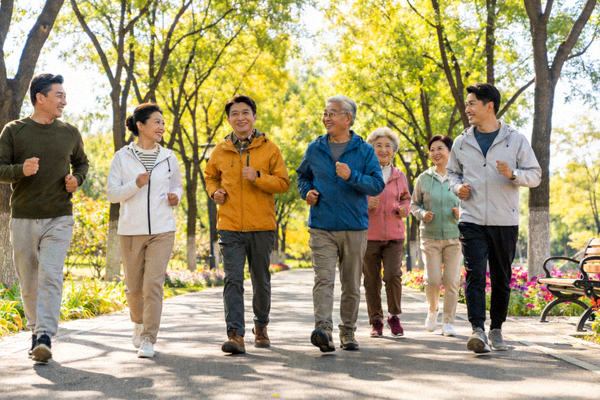 一群不同年龄的人在绿树成荫的公园步道上快乐健步走，有说有笑