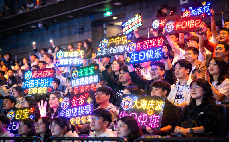 电竞比赛现场观众席全景，观众举着应援灯牌为战队加油